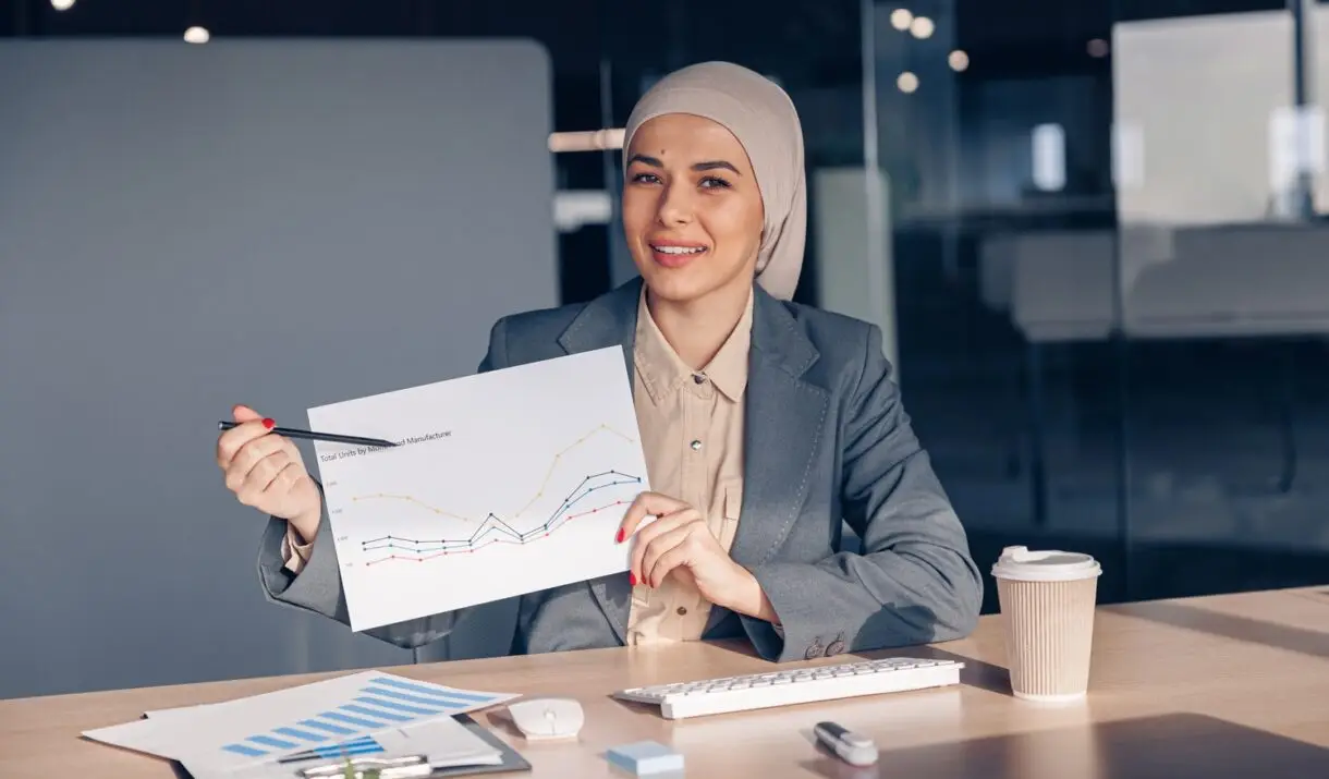 Smiling Muslim Businesswoman In Hijab Shows A Grap AMH74W7 1 1220x715