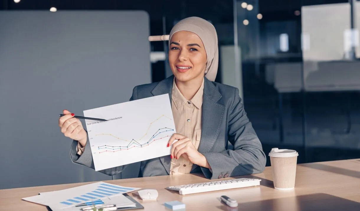 Smiling Muslim Businesswoman In Hijab Shows A Grap AMH74W7 1220x715