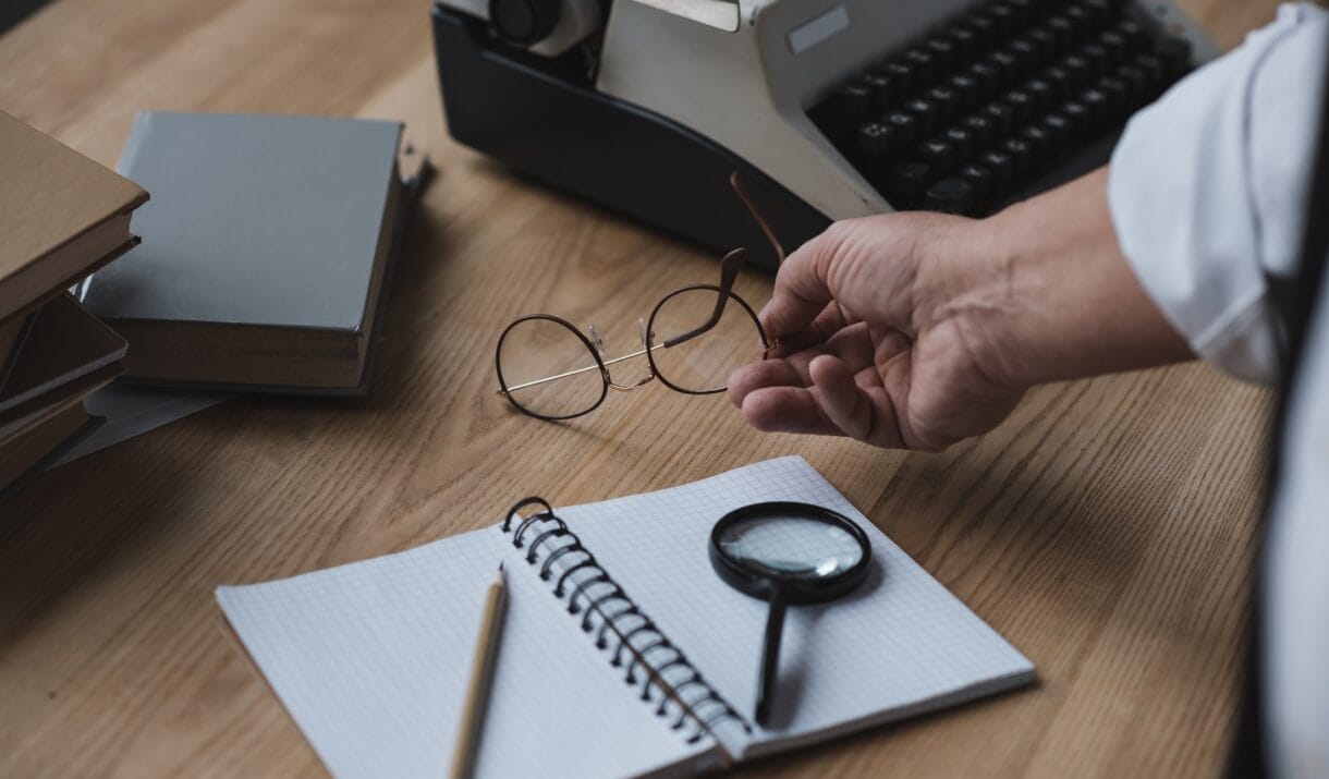 Senior Writer Putting Eyeglasses On Work Desk W7GAV6Z 1220x715