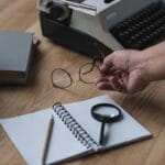 Senior Writer Putting Eyeglasses On Work Desk W7GAV6Z 150x150